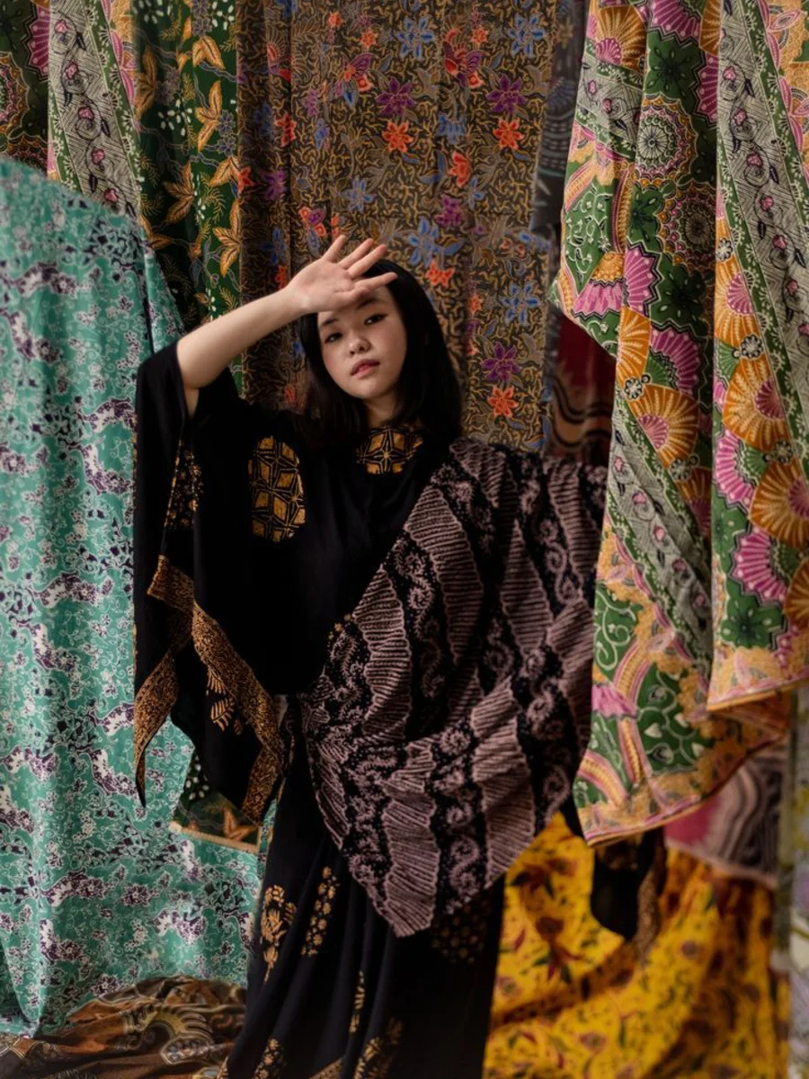 Model mengenakan batik di antara tumpukan kain batik