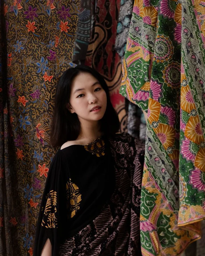 Model duduk di antara tirai kain batik